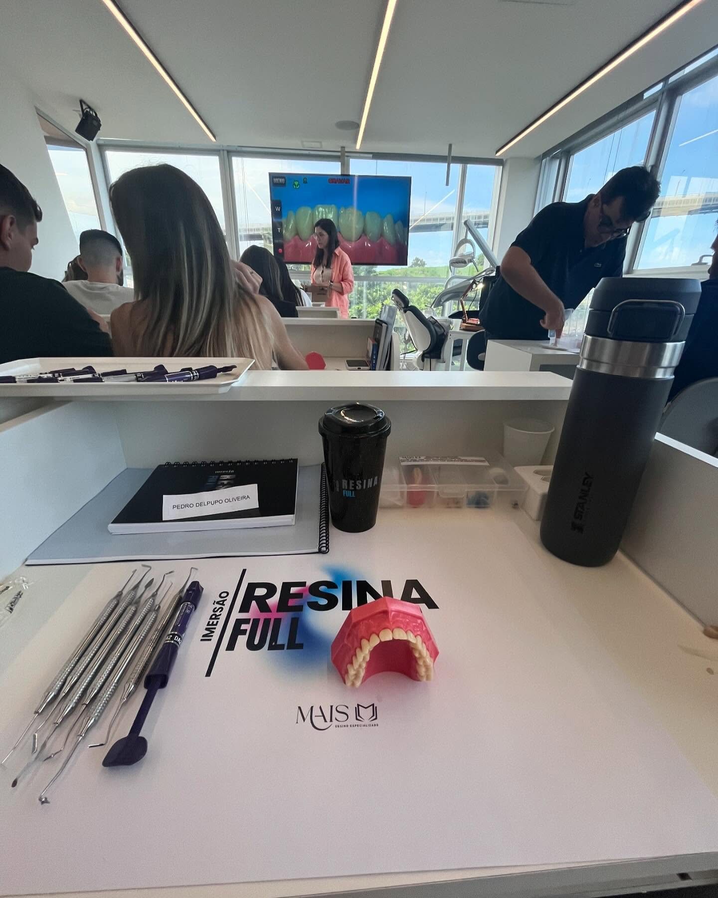 Bancada de um curso de resina: o instrumental, o modelo da arcada em vermelho sobre a bancada e o caderno de anotações.