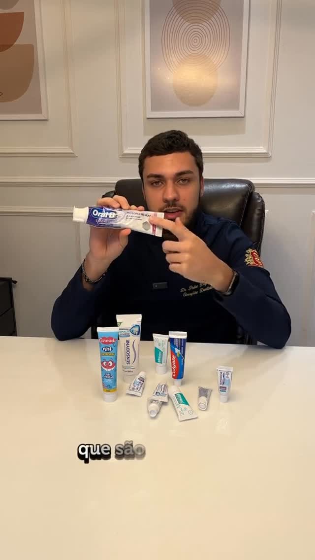 Dr. Pedro Delpupo à mesa segurando um creme dental e apontando, com vários tubos dispostos à frente.